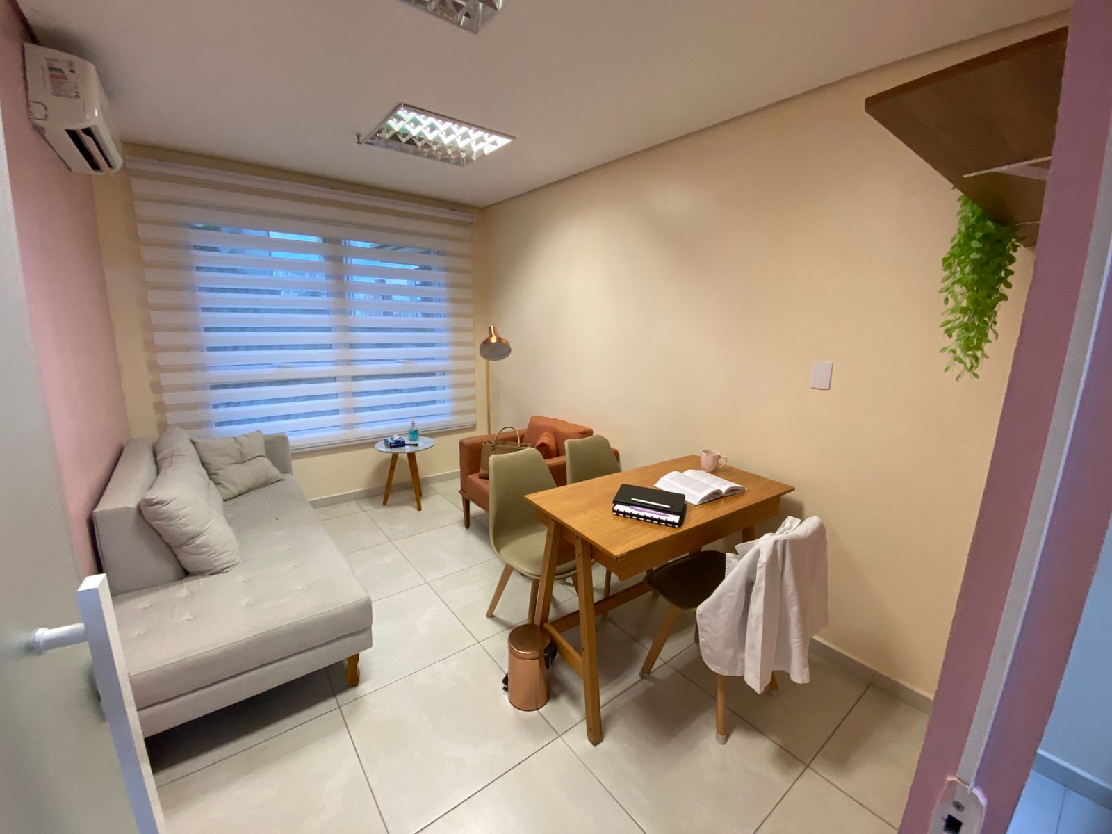 Consultório aconchegante com sofá cinza, poltrona caramelo e mesa de madeira